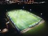 Night time aerial view of Kett's Park floodlit 3G football pitch, looking east.