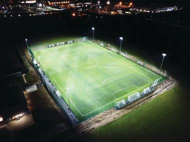 Night time aerial view of Kett's Park floodlit 3G football pitch, looking east.