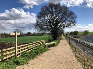 The Bure Valley Path, featuring a bench, a signpost and the steam train line.