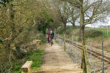Two cyclists travelling down Bure Valley Path, next to the steam train line. 
