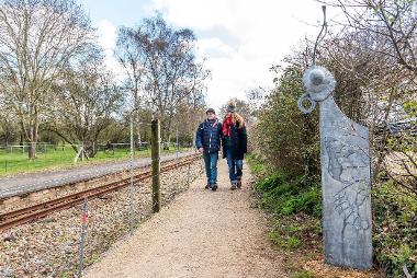 Two pedestrians walking down Bure Valley Path, next to the steam train line. 