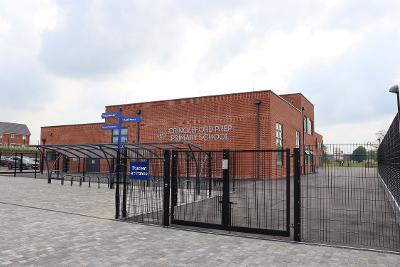 An image of the new school. The image shows a multi-storey red brick building, with black fencing around the outside with cycle parking and signage.