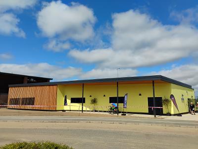 An image of the new Aylsham Gym & Fitness Hub. A yellow rectangular building, with wooden slats. In front of the building are cycle racks and a road.