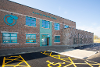 An image of Blofield Primary School's entrance, showing a disabled car parking space outside of the red brick building with blue signage.