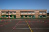 An image of Blofield Primary School's playground with courts outlined, behind the green fence is the school, a red brick building with green windows.